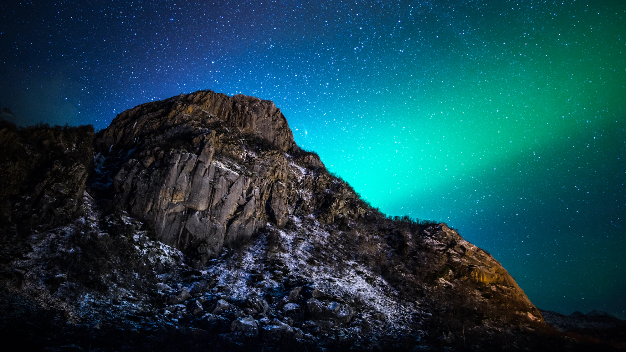 Grünes Polarlicht zieht über eine dunkle, felsige Berglandschaft auf den Lofoten