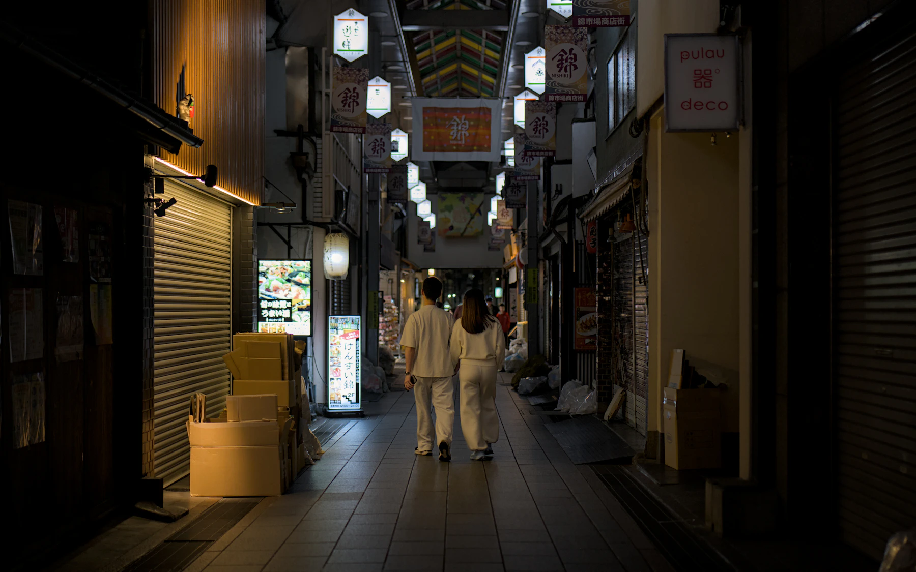 Zwei Menschen gehen durch eine schmale, gedämpft beleuchtete Gasse in Kyoto