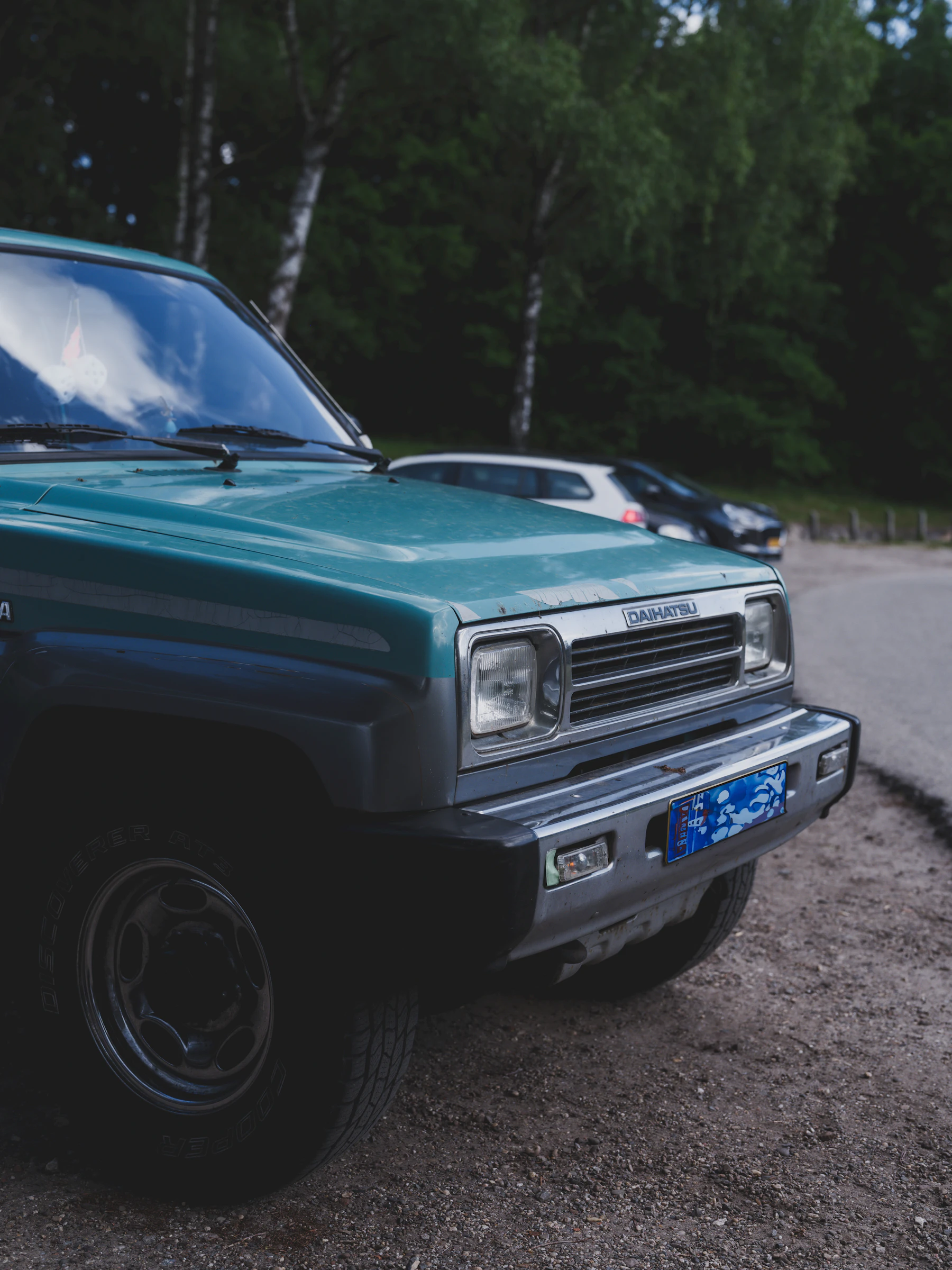 Ein grüner Oldtimer steht mit sichtbaren Gebrauchsspuren am Rand einer Straße